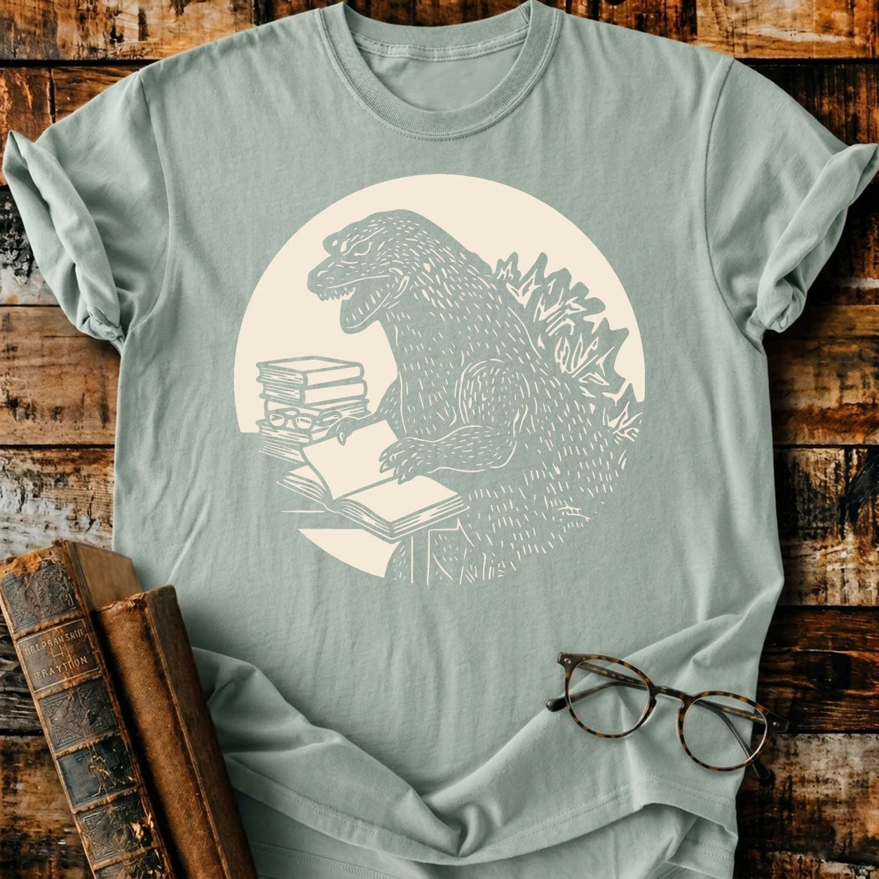 Light green Comfort Colors 1717 t-shirt with a Godzilla monster reading books design.